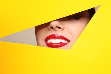 Photo of View of beautiful young woman with red lips through cutout in color paper, closeup