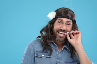 Stylish hippie man smoking cigarette on light blue background