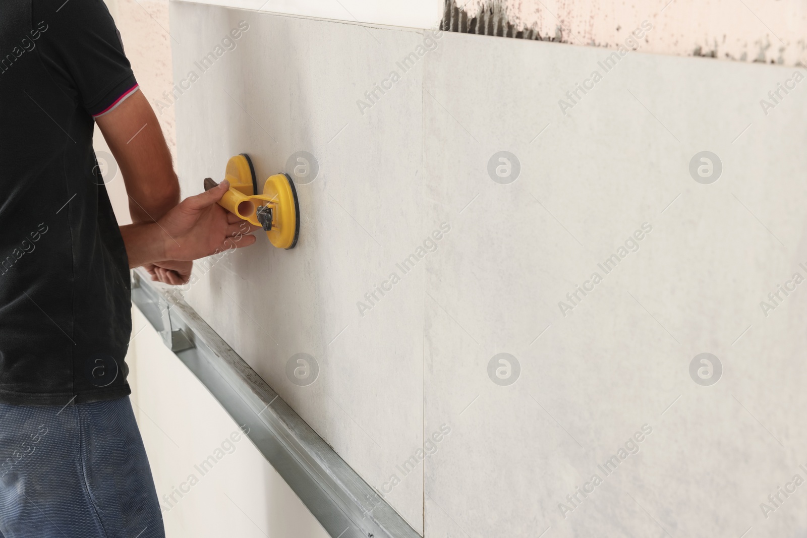 Photo of Worker installing wall tiles with vacuum holder indoors, closeup