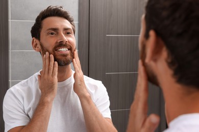 Smiling bearded man looking at mirror in bathroom