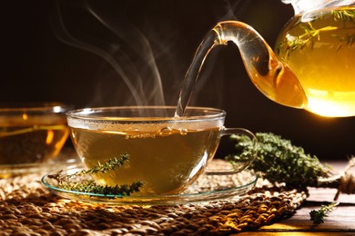 Photo of Pouring aromatic herbal tea into cup and thyme on wooden table
