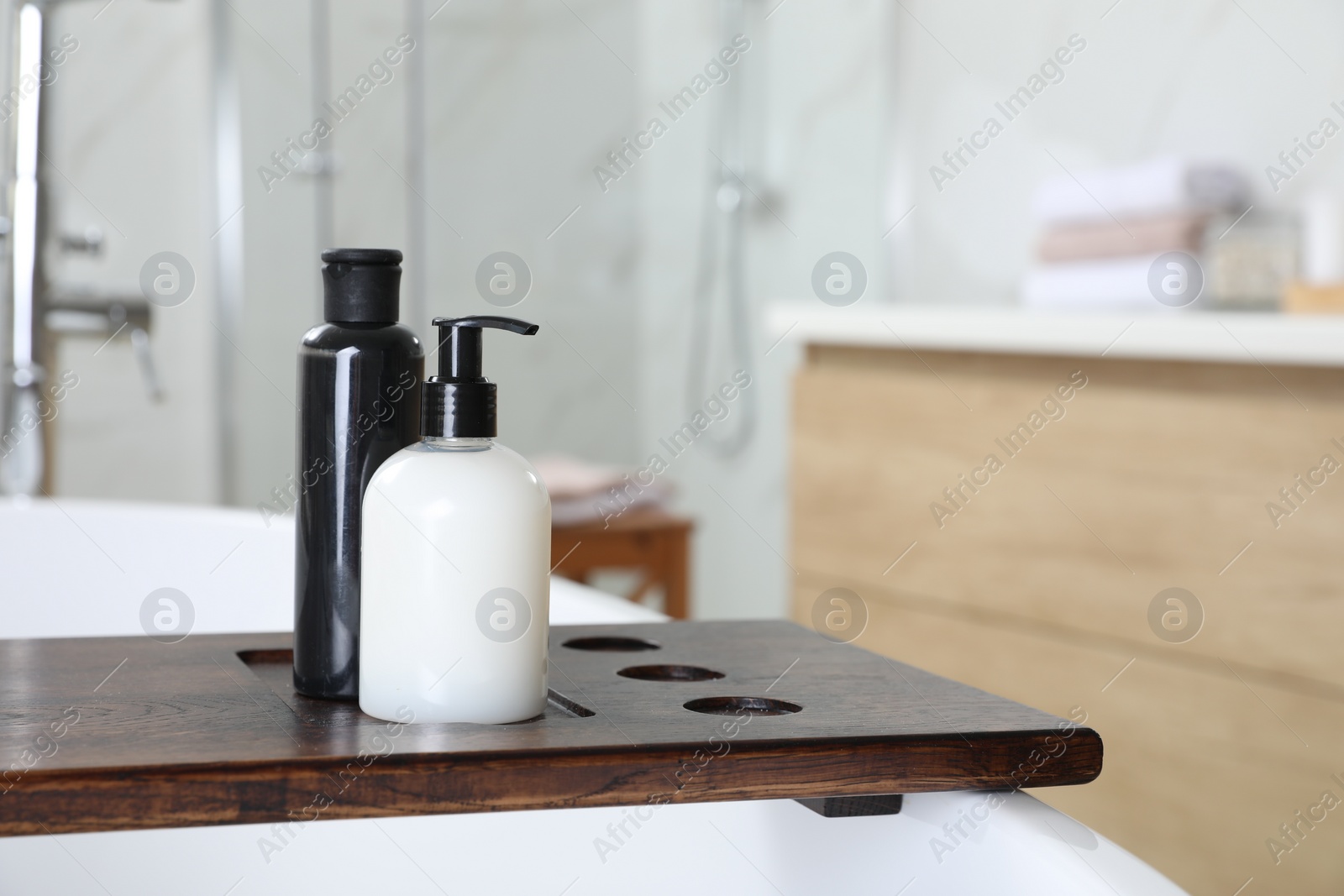 Photo of Wooden bath tray with bottles of shower gels on tub indoors, space for text