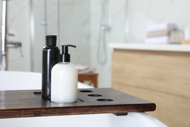 Wooden bath tray with bottles of shower gels on tub indoors, space for text