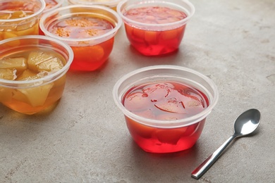 Photo of Plastic containers with tasty jelly desserts and spoon on grey table