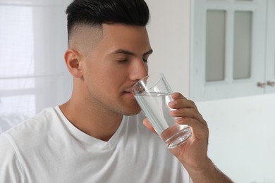 Man drinking tap water from glass at home, closeup