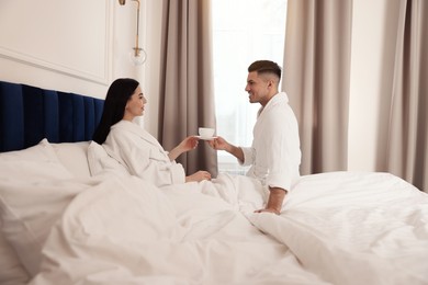 Photo of Happy couple wearing bathrobes resting on bed in hotel room