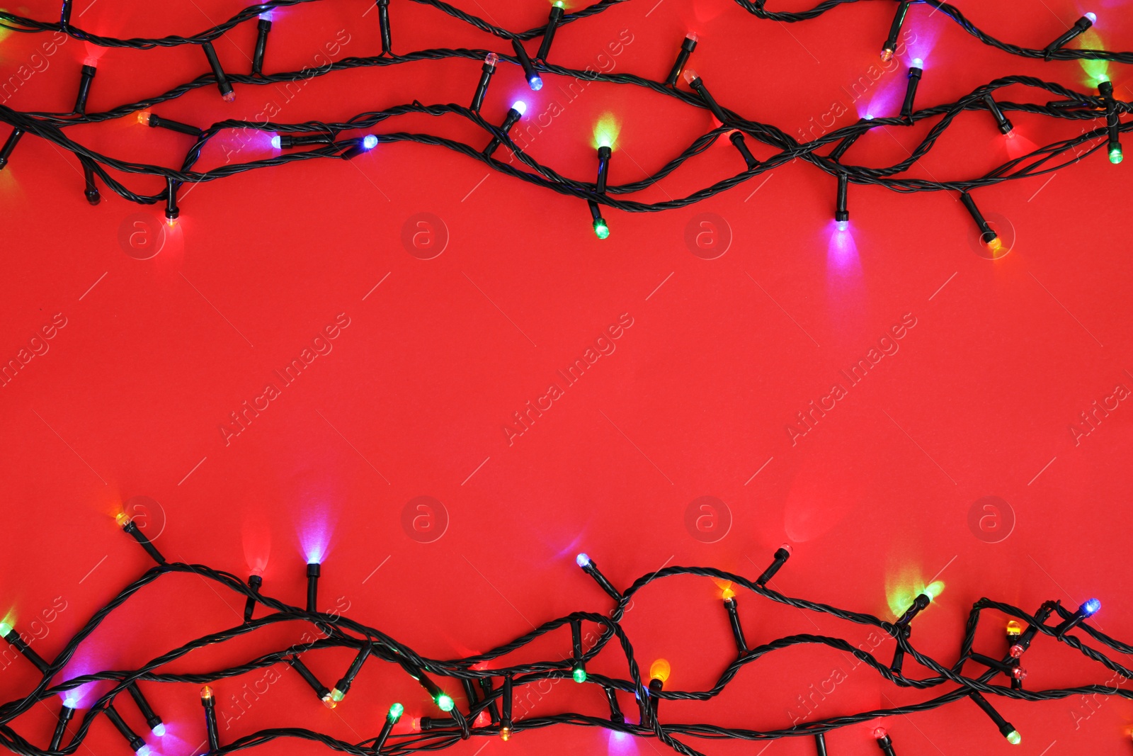 Photo of Glowing Christmas lights on color background, top view