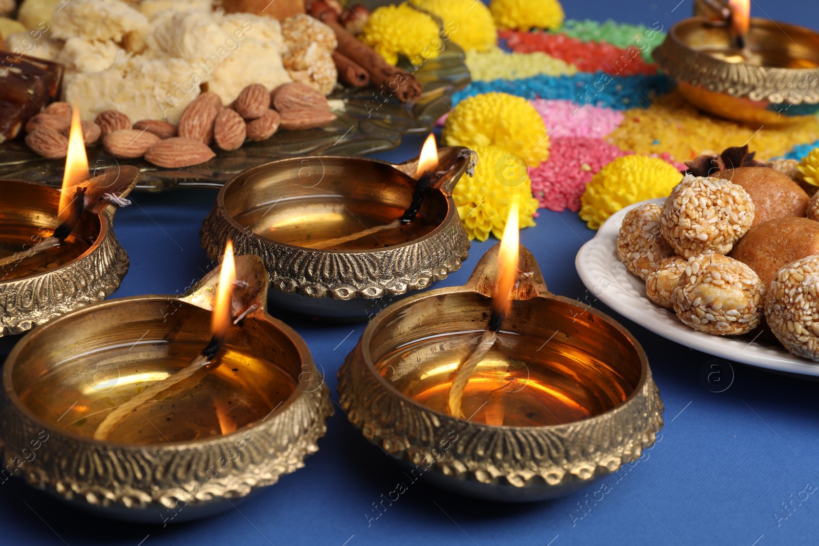 Photo of Diwali celebration. Tasty Indian sweets, diya lamps and colorful rangoli on blue table, closeup