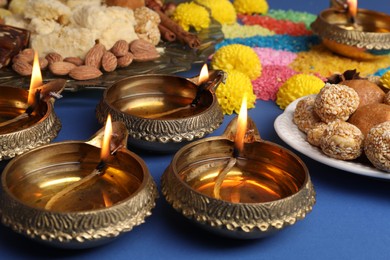 Photo of Diwali celebration. Tasty Indian sweets, diya lamps and colorful rangoli on blue table, closeup