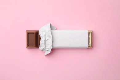 Tasty chocolate bar in package on pink background, top view