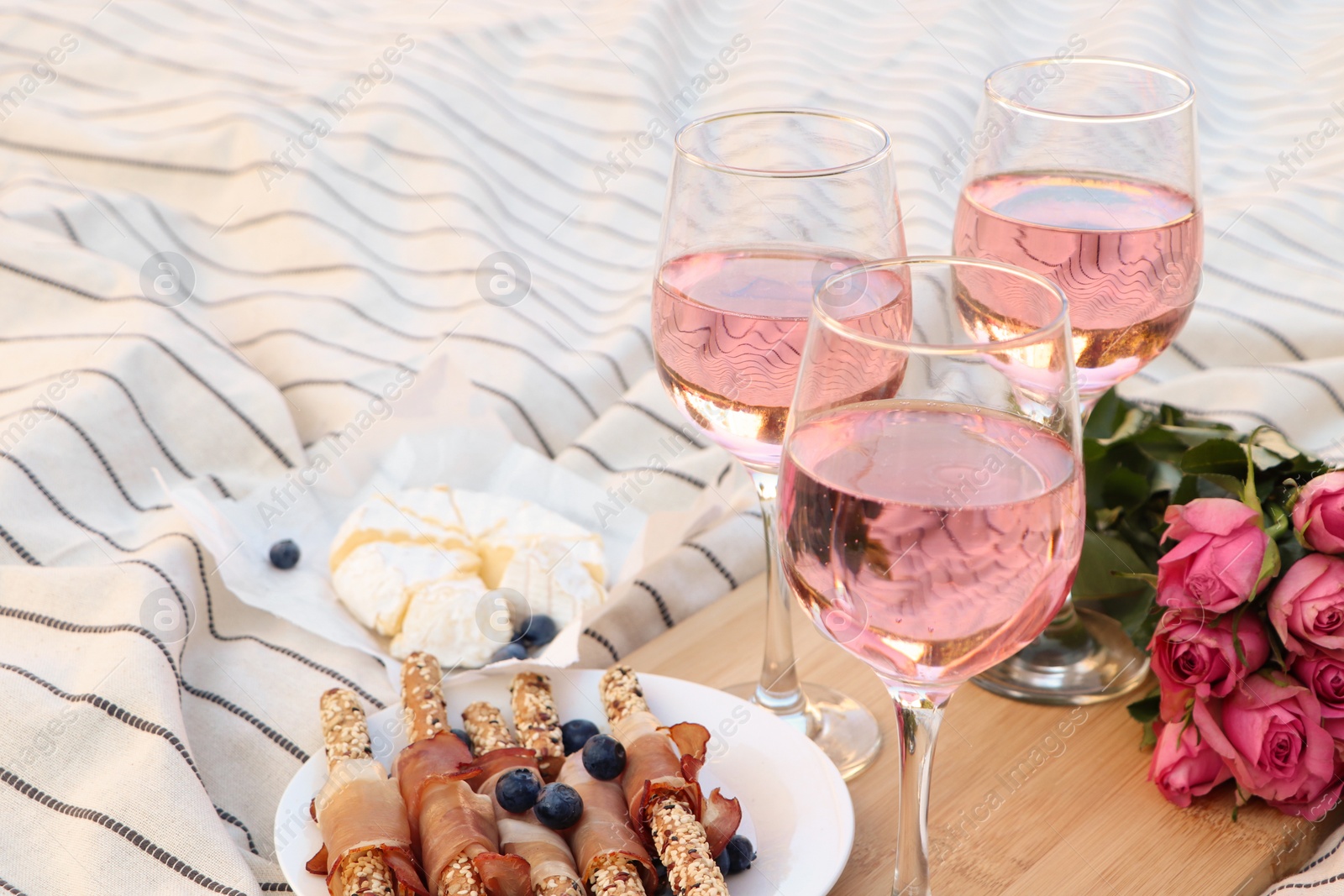 Photo of Glasses of delicious rose wine, flowers and food on white picnic blanket