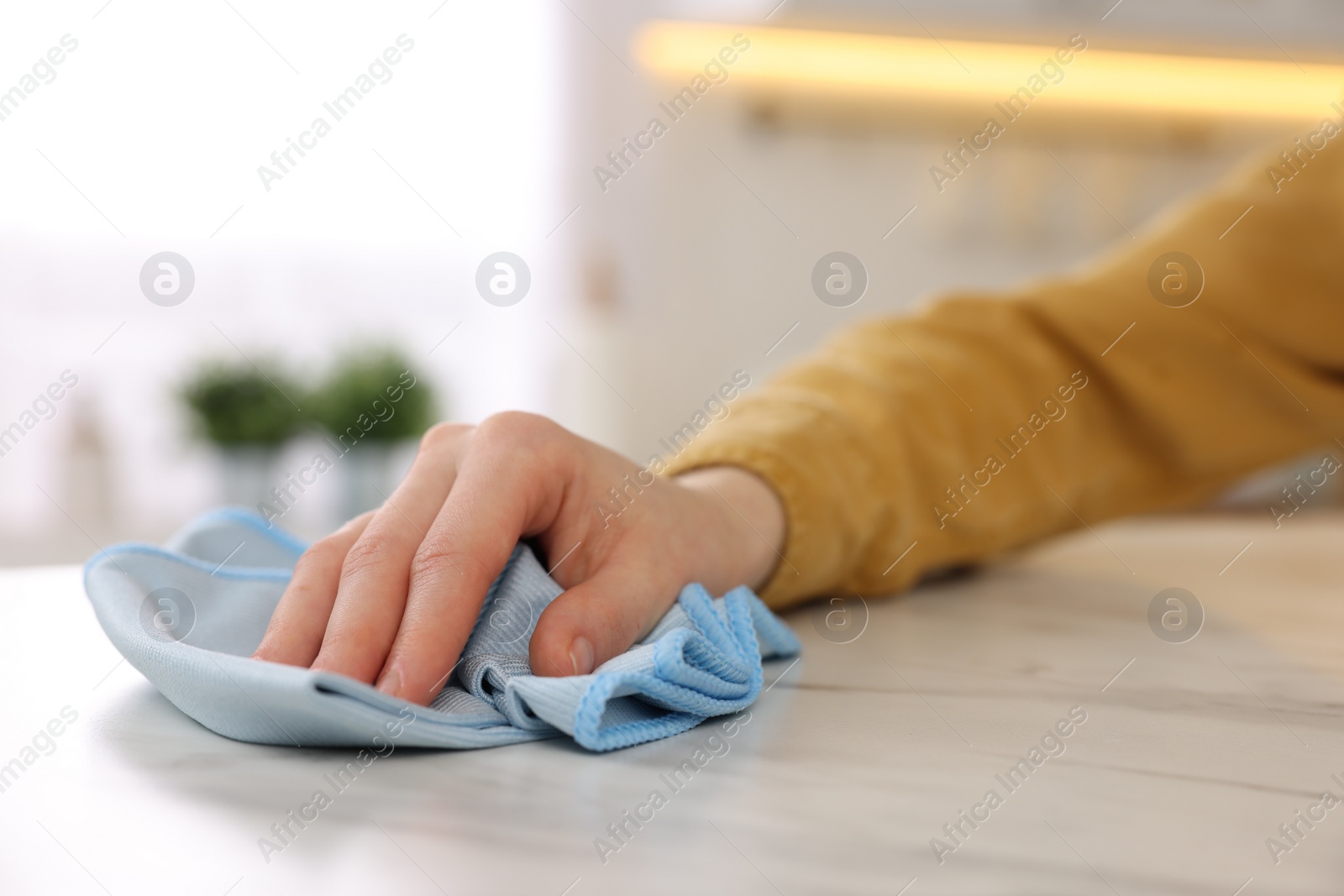 Photo of Woman with microfiber cloth cleaning white marble table in kitchen, closeup