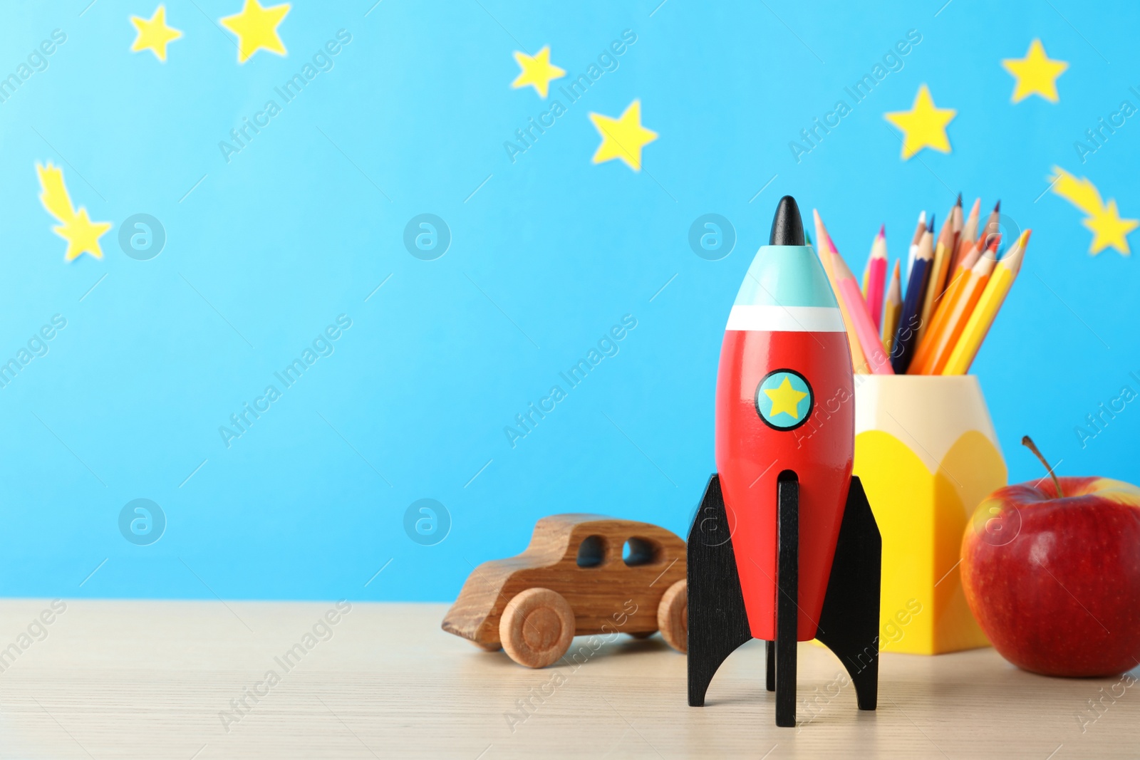 Photo of Rocket, pencils, toy car and apple on wooden table, space for text. Back to school