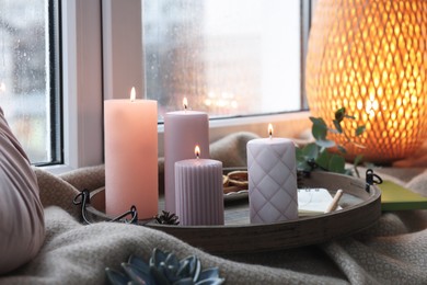 Tray with burning wax candles and decor on window sill indoors