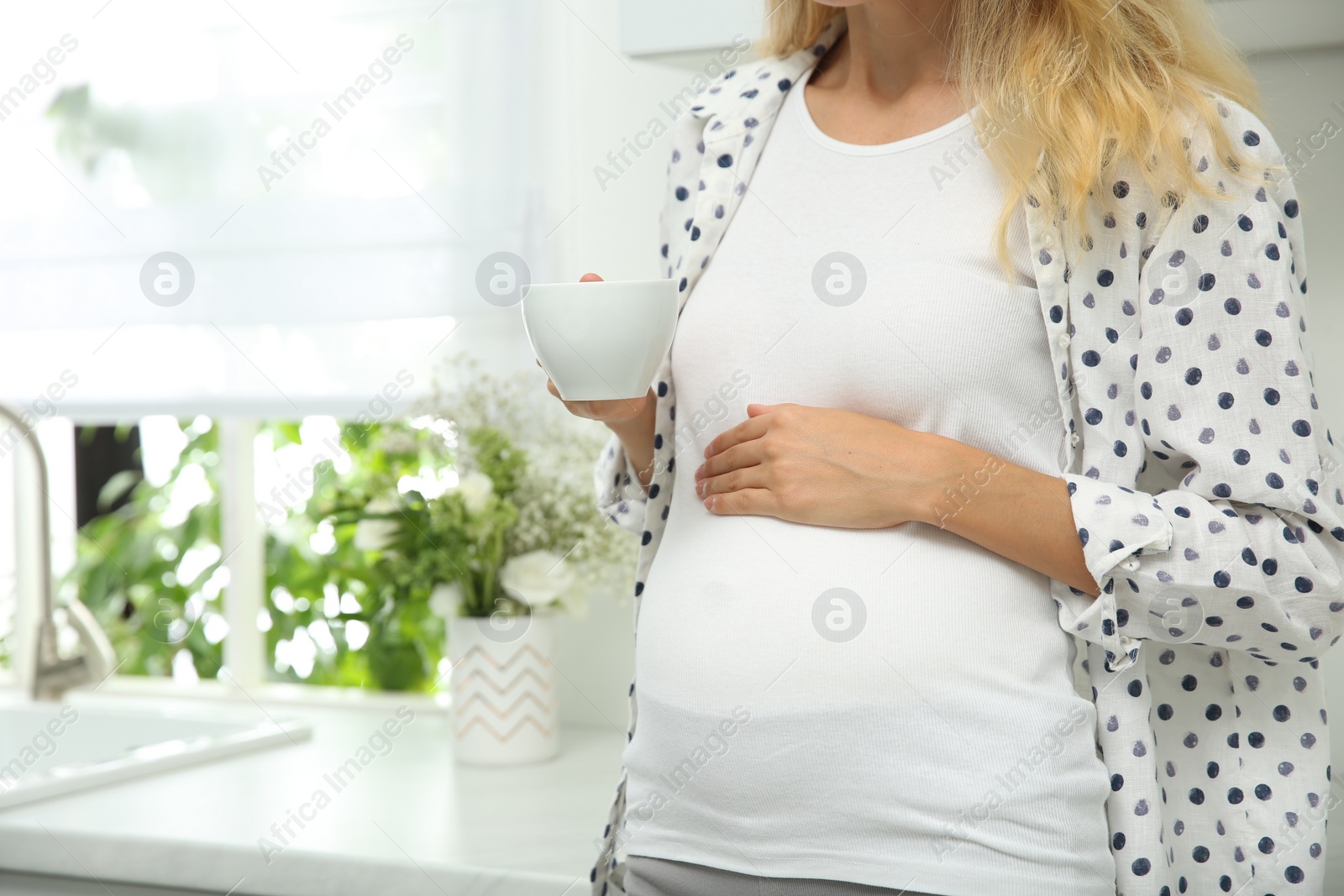 Photo of Beautiful pregnant woman drinking tea in kitchen, closeup