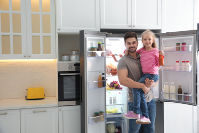 Young father with daughter near open refrigerator in kitchen
