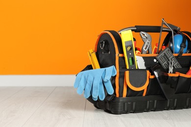Photo of Bag with different tools for repair on floor near orange wall. Space for text