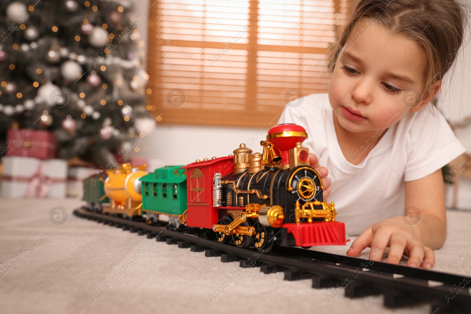 Photo of Little girl playing with colorful train toy in room decorated for Christmas