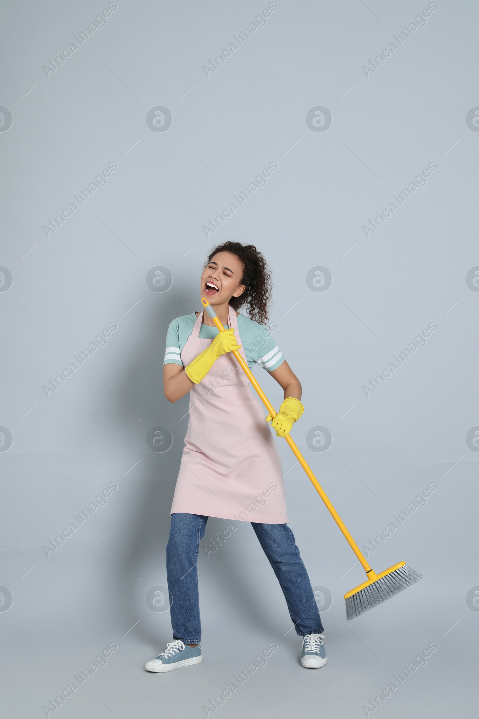 Photo of African American woman with yellow broom singing on grey background