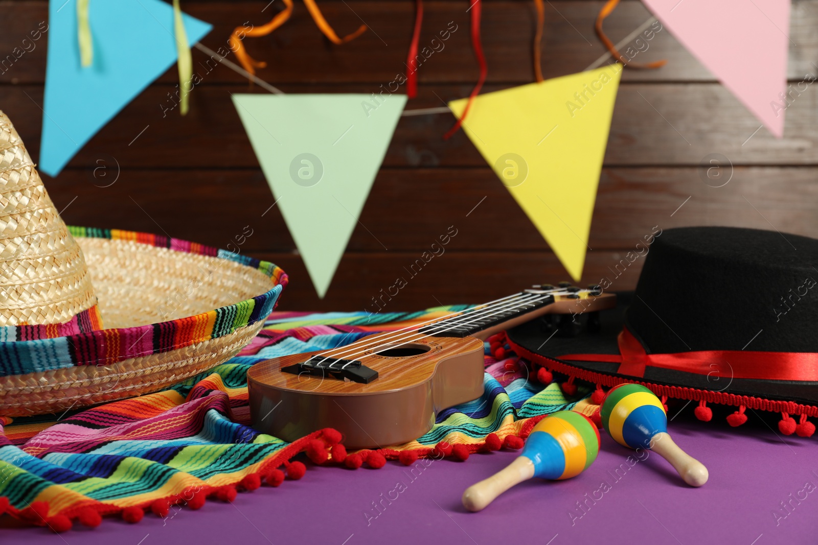 Photo of Mexican sombrero and black Flamenco hats, ukulele and maracas on purple table, closeup