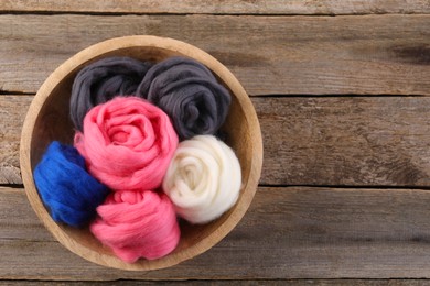 Photo of Colorful felting wool in bowl on wooden table, top view. Space for text