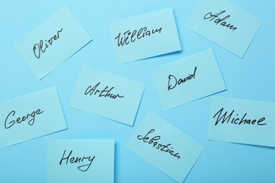 Photo of Choosing baby name. Paper stickers with different names on light blue background, flat lay