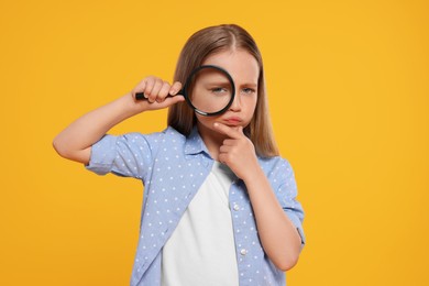 Cute little girl looking through magnifier on yellow background