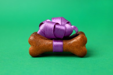 Bone shaped dog cookies with purple bow on green background, closeup