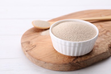 Bowl and spoon with active dry yeast on white wooden table