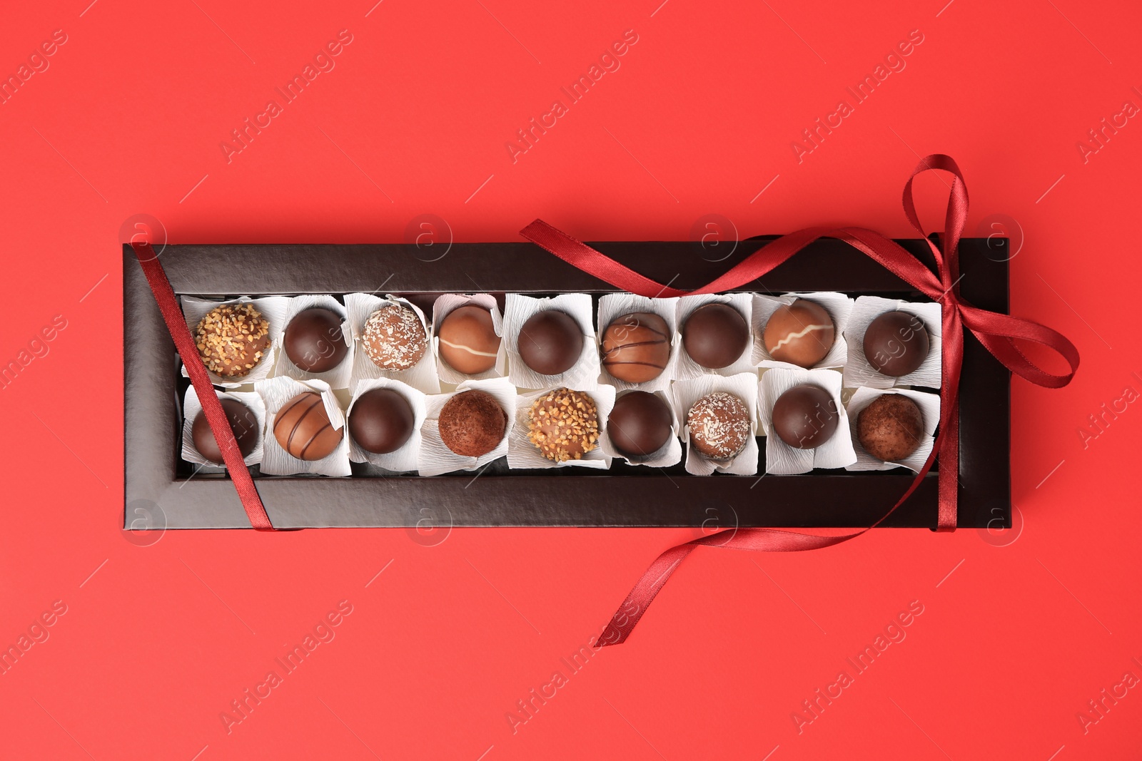 Photo of Box with delicious chocolate candies on red table, top view
