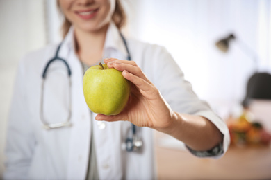 Photo of Nutritionist with fresh apple in her office, closeup