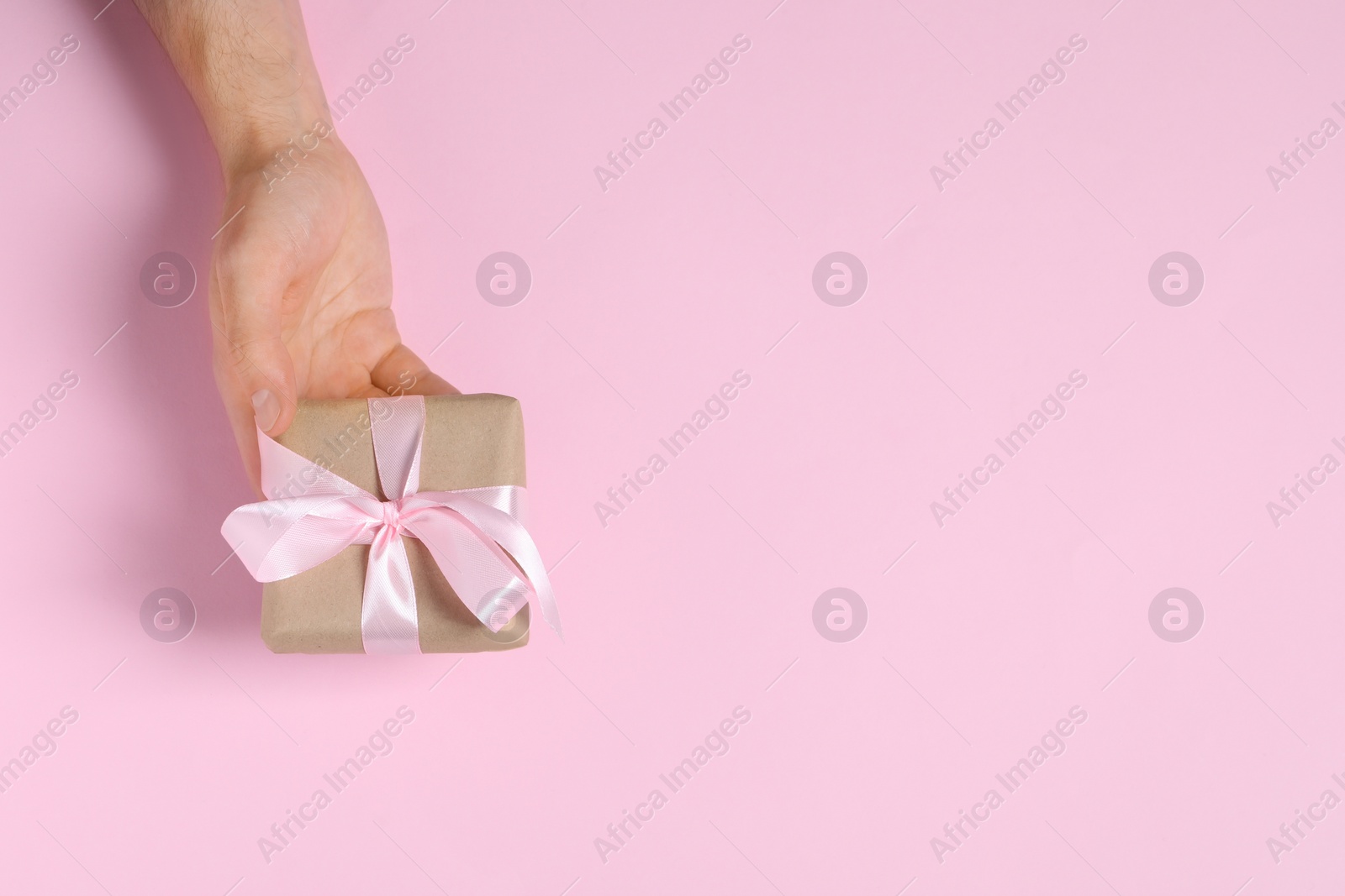 Photo of Man holding gift box with bow on pink background, top view. Space for text