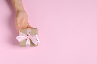 Photo of Man holding gift box with bow on pink background, top view. Space for text