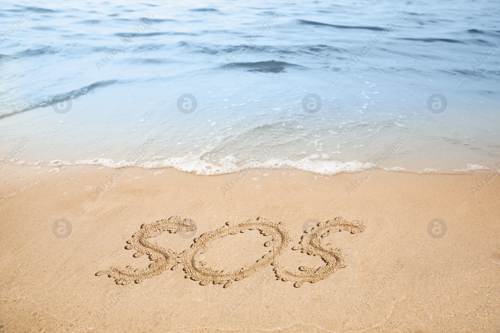 Image of SOS message drawn on sandy beach near sea