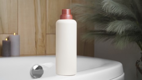 Photo of Beige bottle of bubble bath and candles on tub indoors