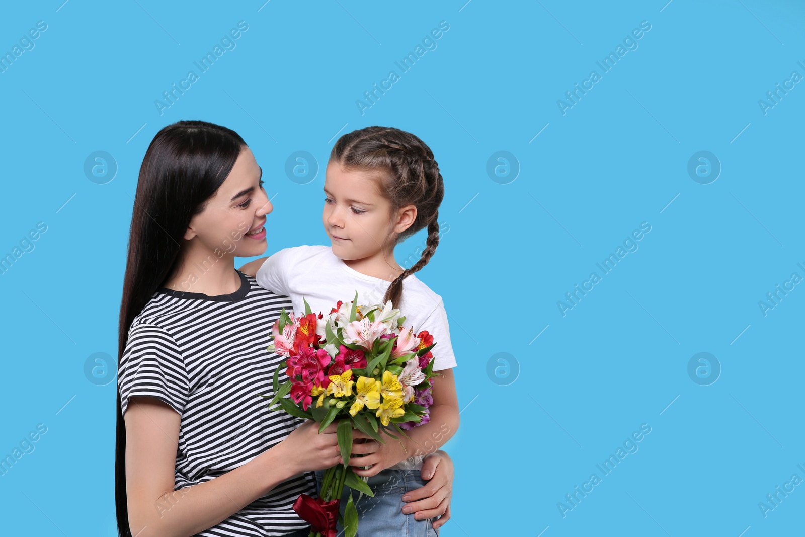 Photo of Happy woman with her daughter and bouquet of beautiful flowers on light blue background, space for text. Mother's day celebration