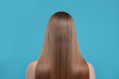 Photo of Woman with healthy hair on light blue background, back view