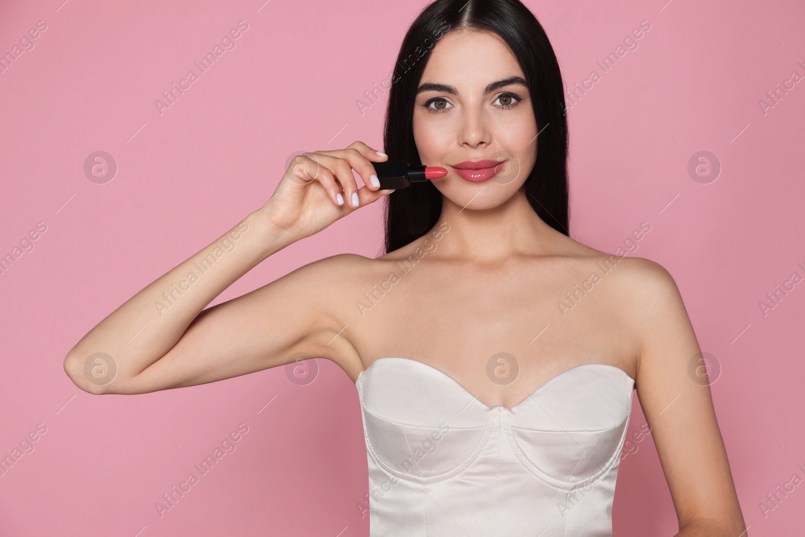 Photo of Young woman with beautiful makeup holding glossy lipstick on pink background