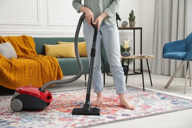 Woman cleaning carpet with vacuum cleaner at home, closeup