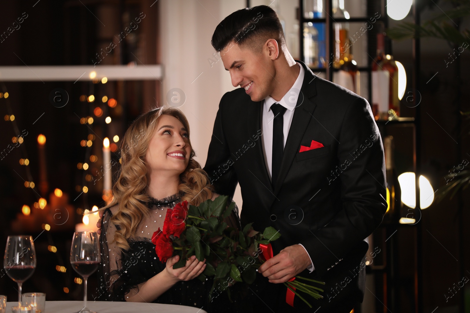 Photo of Man presenting roses to his beloved woman in restaurant at Valentine's day dinner