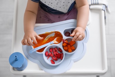 Photo of Little baby eating food in high chair at kitchen, closeup. Top view