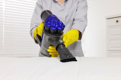 Photo of Woman in gloves disinfecting mattress with vacuum cleaner indoors, closeup