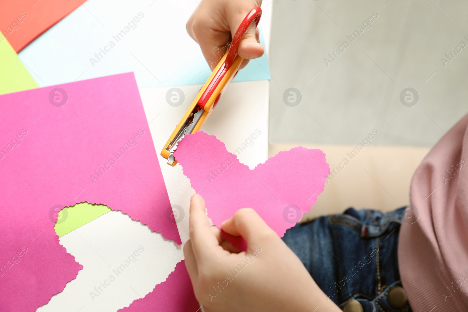 Photo of Child cutting out paper heart with craft scissors at table, closeup