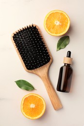 Photo of Wooden hair brush, bottle of essential oil and orange slices on white marble table, flat lay