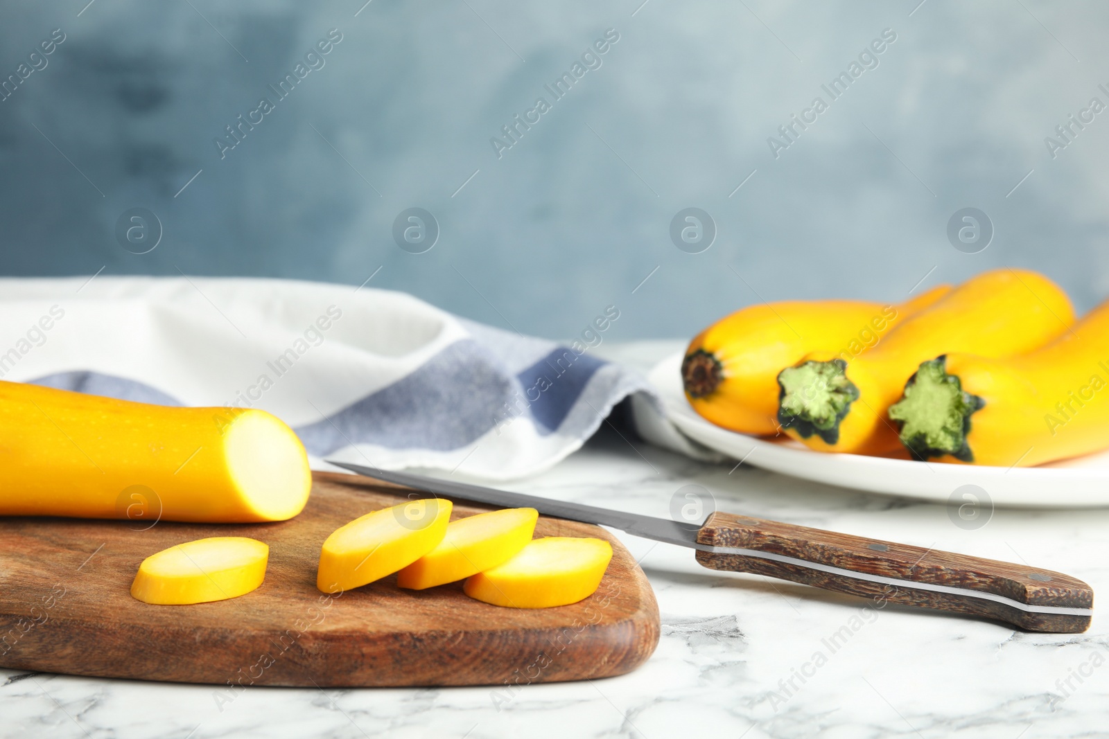 Photo of Fresh ripe yellow zucchinis on marble table against blue background, space for text