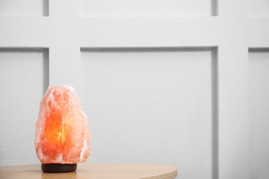 Himalayan salt lamp on wooden table indoors. Space for text