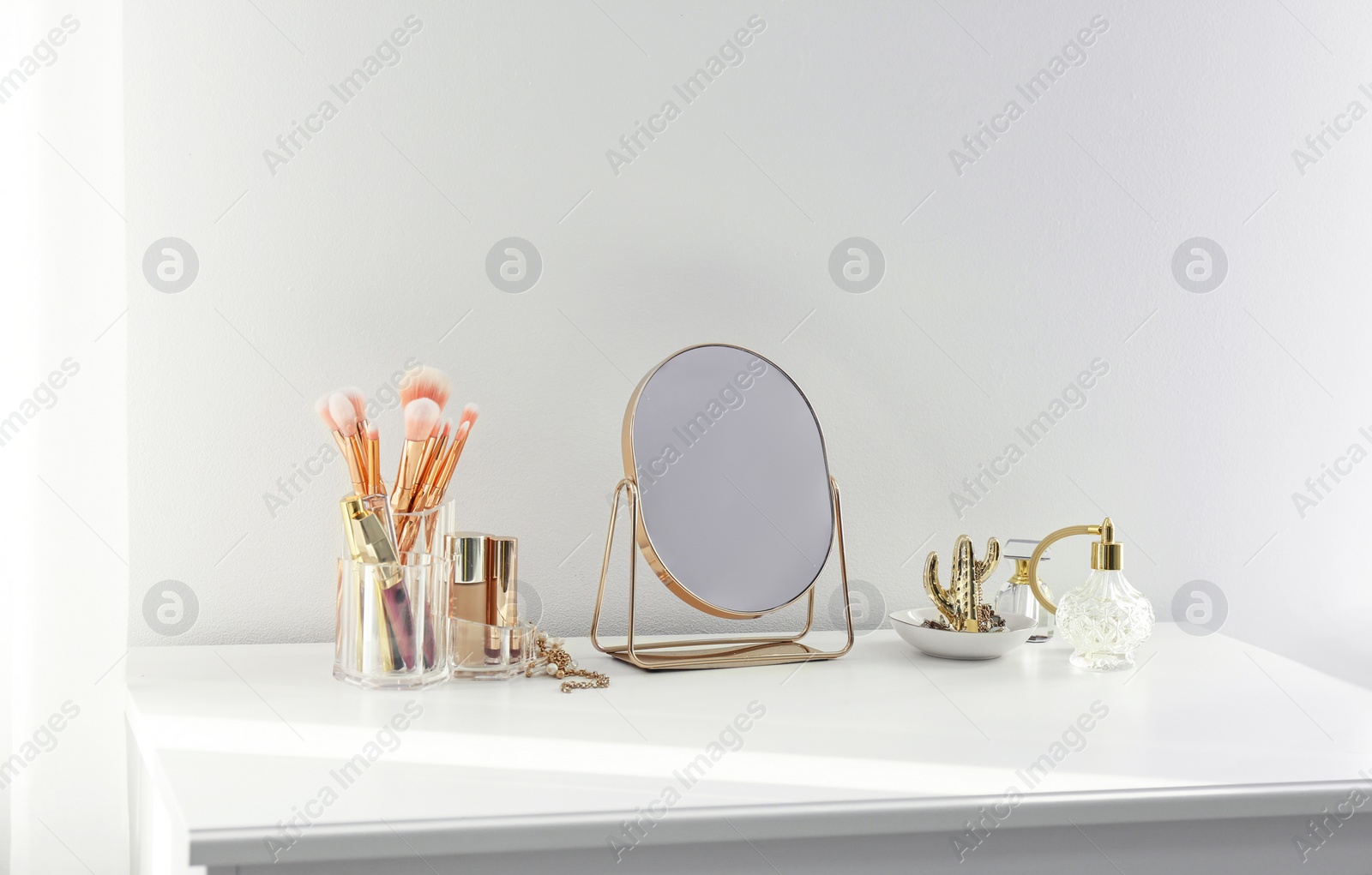 Photo of Small mirror and makeup products on white dressing table indoors