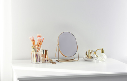 Photo of Small mirror and makeup products on white dressing table indoors