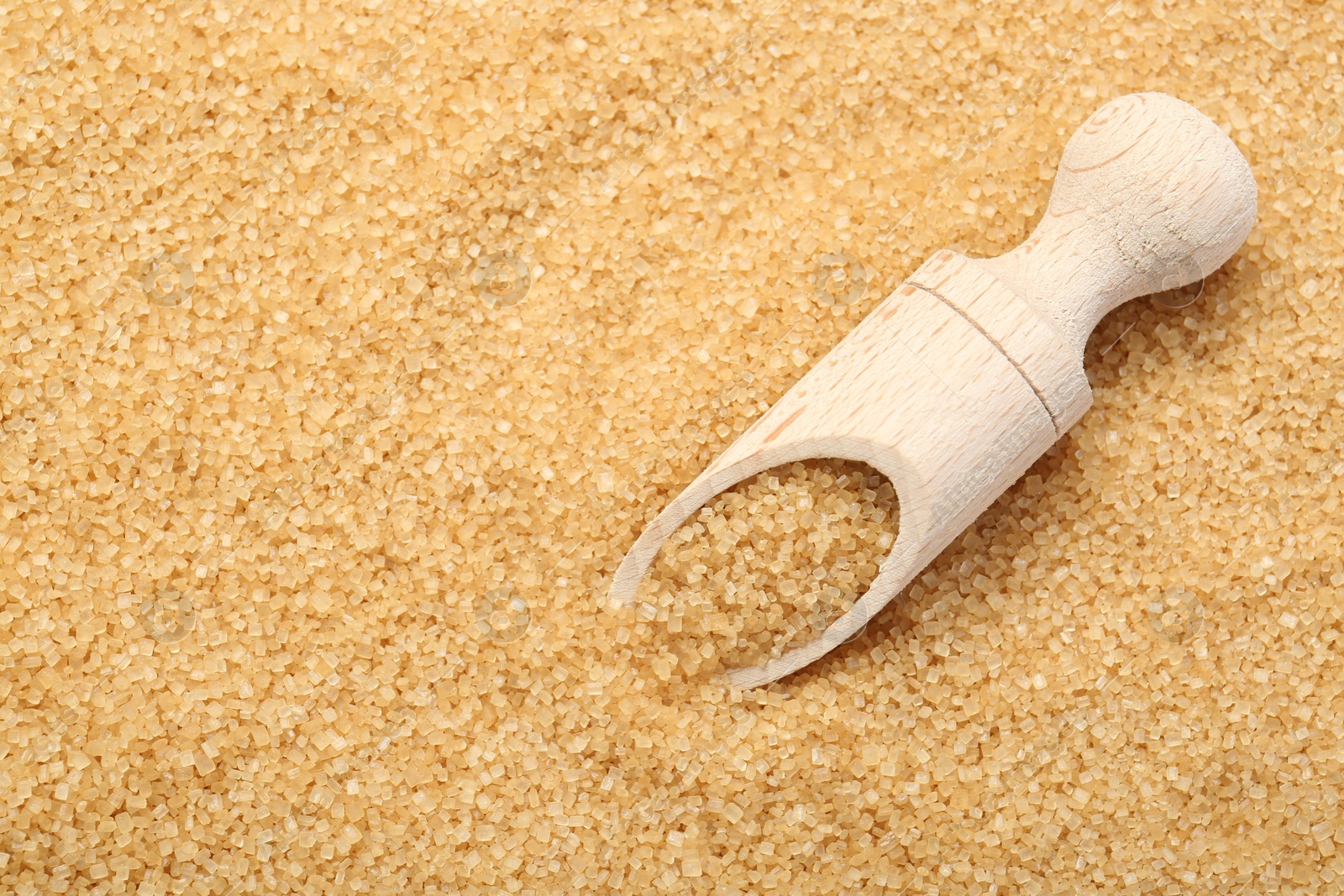 Photo of Wooden scoop on granulated brown sugar, top view