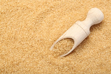 Wooden scoop on granulated brown sugar, top view